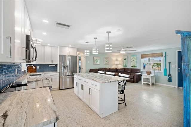 kitchen featuring appliances with stainless steel finishes, decorative backsplash, white cabinetry, a center island, and ceiling fan