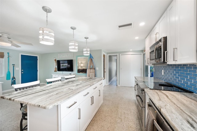 kitchen with range, light stone countertops, tasteful backsplash, pendant lighting, and white cabinets