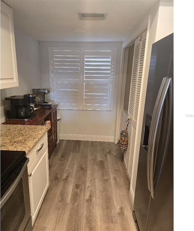 kitchen with stainless steel appliances, light stone countertops, light wood-type flooring, and white cabinetry