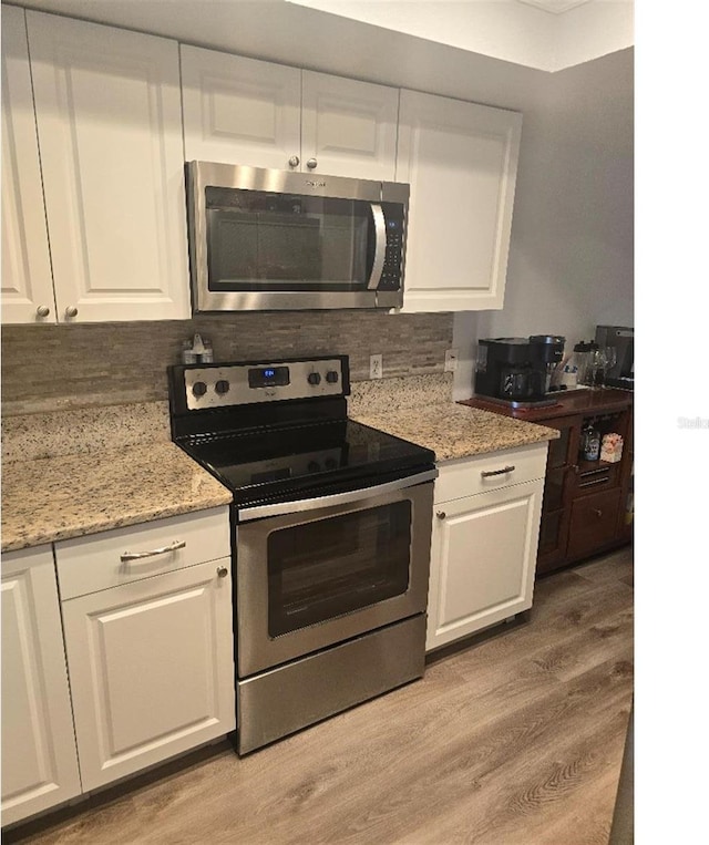 kitchen featuring light wood-type flooring, light stone countertops, stainless steel appliances, and white cabinetry