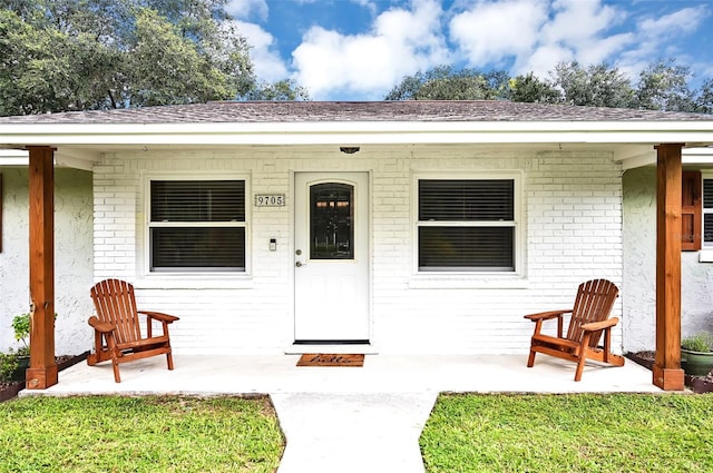 doorway to property featuring covered porch and brick siding