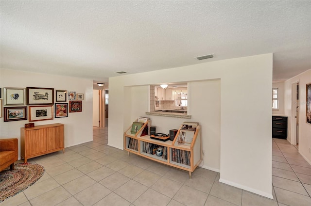 interior space featuring baseboards, visible vents, a textured ceiling, and light tile patterned flooring