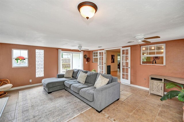 living area with ceiling fan, french doors, light tile patterned floors, and baseboards