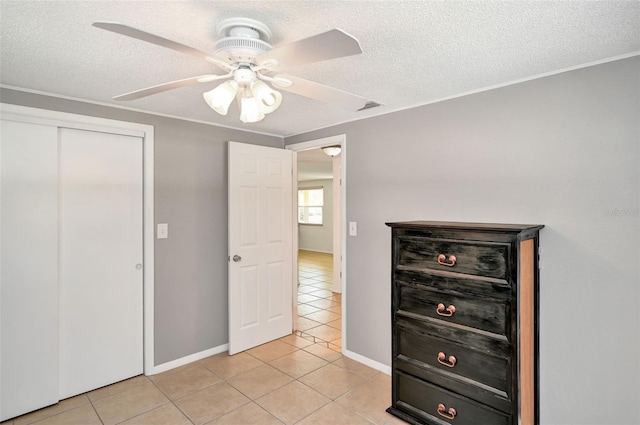 unfurnished bedroom with a textured ceiling, ceiling fan, light tile patterned flooring, baseboards, and a closet