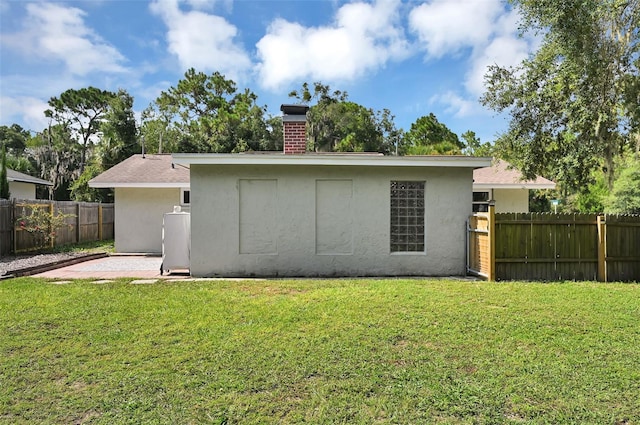 rear view of property with a chimney, fence, a yard, a patio area, and stucco siding