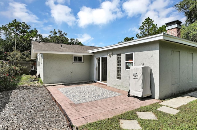 rear view of property featuring roof with shingles, a patio area, fence, and stucco siding