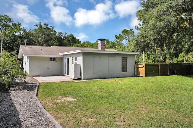 back of property featuring fence, a yard, stucco siding, a chimney, and a patio area