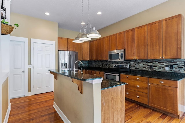 kitchen featuring dark stone counters, backsplash, appliances with stainless steel finishes, hardwood / wood-style flooring, and a center island with sink