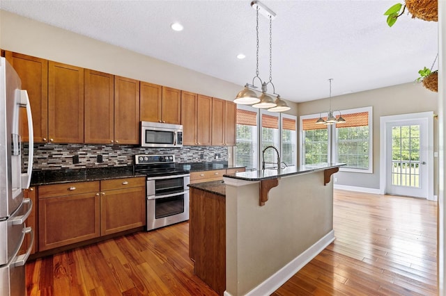 kitchen featuring appliances with stainless steel finishes, light hardwood / wood-style flooring, a center island with sink, and tasteful backsplash