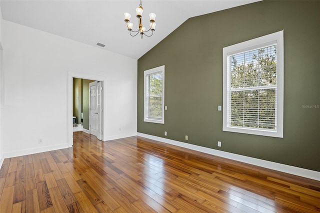 empty room with a notable chandelier, vaulted ceiling, hardwood / wood-style floors, and a healthy amount of sunlight