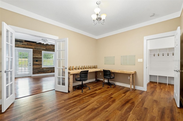 office featuring french doors, wooden walls, ceiling fan with notable chandelier, built in desk, and wood-type flooring