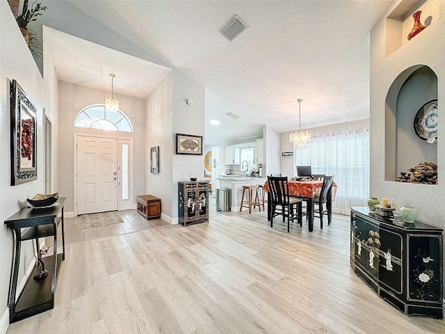 foyer with baseboards, visible vents, light wood-style flooring, a textured ceiling, and a notable chandelier