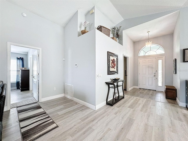 entryway featuring baseboards, visible vents, light wood finished floors, and high vaulted ceiling