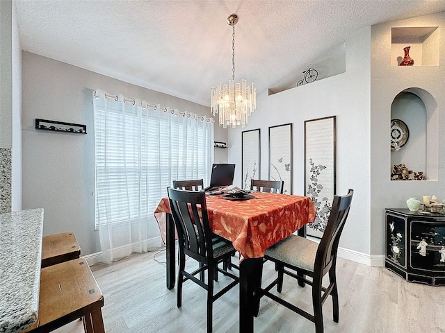 dining space featuring a textured ceiling, light hardwood / wood-style flooring, lofted ceiling, and a chandelier