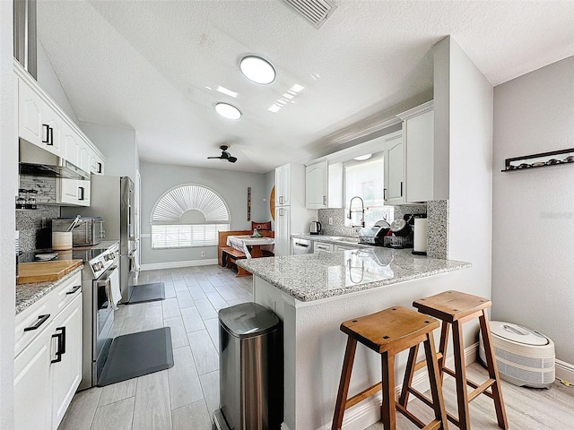 kitchen with a kitchen bar, visible vents, light stone counters, a peninsula, and decorative backsplash