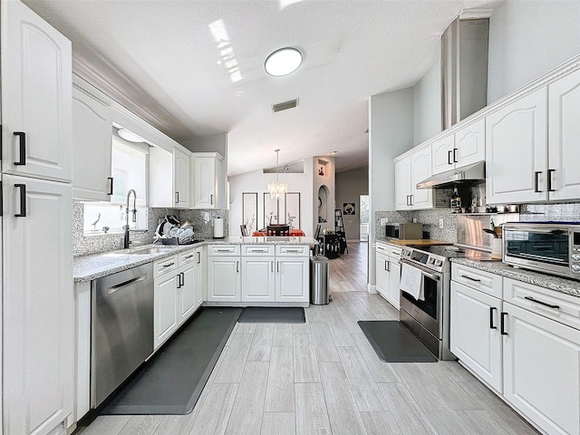 kitchen featuring visible vents, a peninsula, a sink, under cabinet range hood, and appliances with stainless steel finishes