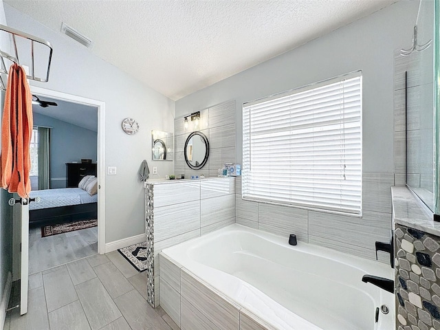 bathroom with tiled tub, vanity, hardwood / wood-style floors, vaulted ceiling, and a textured ceiling