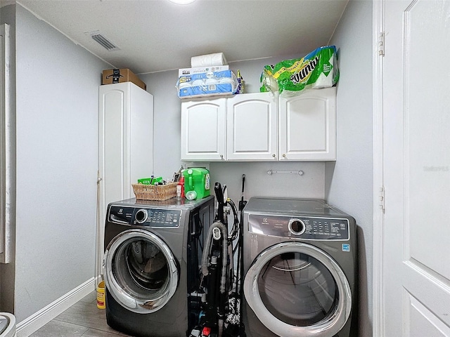 washroom featuring visible vents, wood finished floors, washing machine and dryer, cabinet space, and baseboards