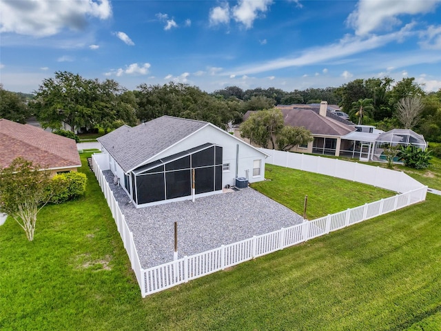 back of house featuring central air condition unit, a lawn, a fenced backyard, roof with shingles, and a sunroom