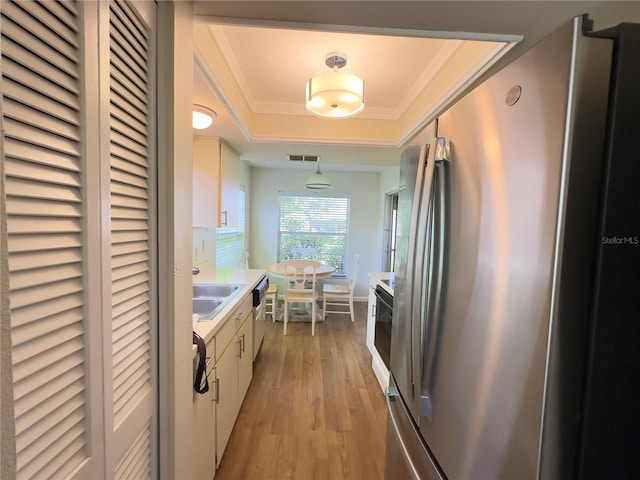 kitchen with appliances with stainless steel finishes, light hardwood / wood-style floors, white cabinetry, sink, and a tray ceiling