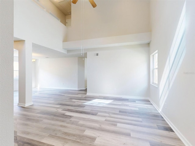 empty room featuring a towering ceiling, light hardwood / wood-style flooring, and ceiling fan