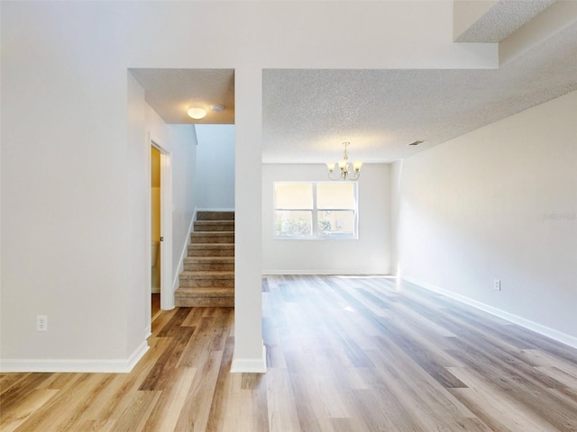 unfurnished room featuring a textured ceiling, light hardwood / wood-style flooring, and a chandelier