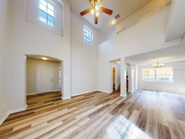 unfurnished living room featuring plenty of natural light, a towering ceiling, ceiling fan with notable chandelier, and light hardwood / wood-style floors