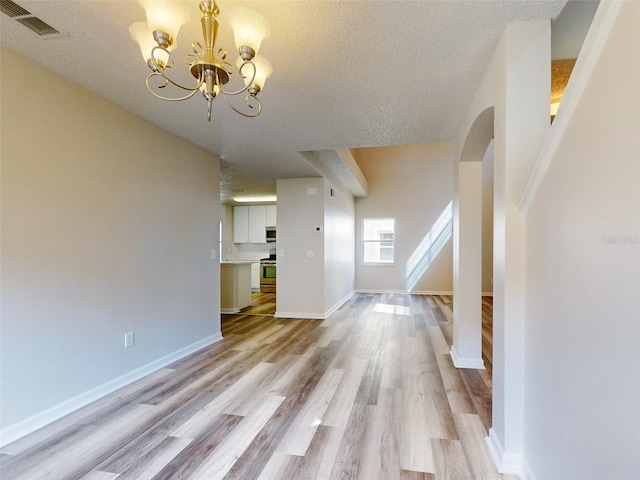 unfurnished living room featuring a textured ceiling, an inviting chandelier, and light wood-type flooring