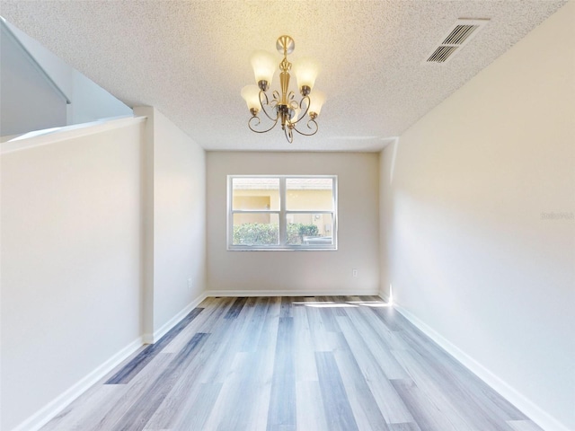 unfurnished room featuring a chandelier, a textured ceiling, and light hardwood / wood-style flooring