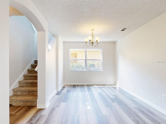 unfurnished room featuring a textured ceiling, a chandelier, and light hardwood / wood-style floors