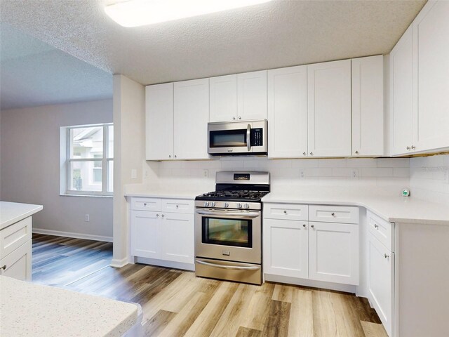 kitchen with a textured ceiling, stainless steel appliances, white cabinets, and light hardwood / wood-style floors