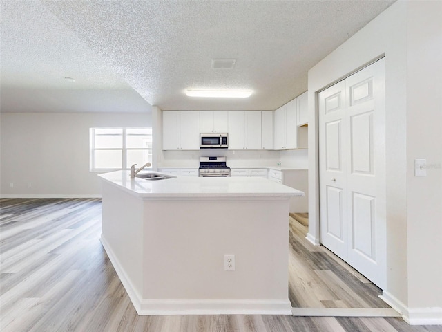 kitchen featuring stainless steel appliances, light wood-type flooring, white cabinets, and a kitchen island with sink