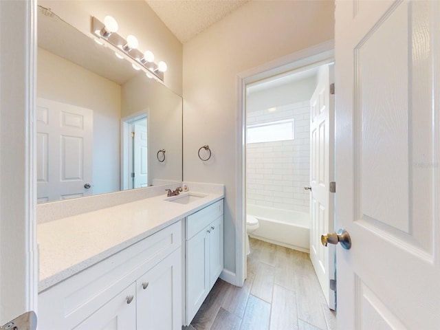 full bathroom with tiled shower / bath, vanity, toilet, and a textured ceiling