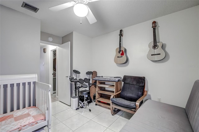 tiled bedroom featuring a nursery area and ceiling fan