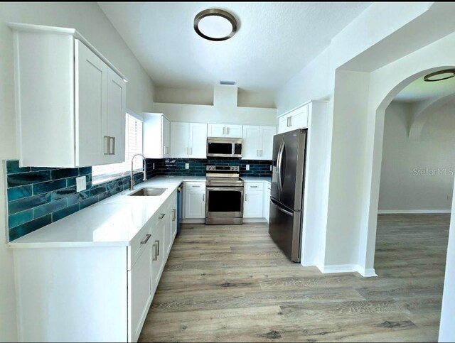 kitchen with sink, appliances with stainless steel finishes, decorative backsplash, light hardwood / wood-style floors, and white cabinetry