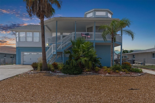 raised beach house featuring an attached garage, stairs, a porch, and concrete driveway