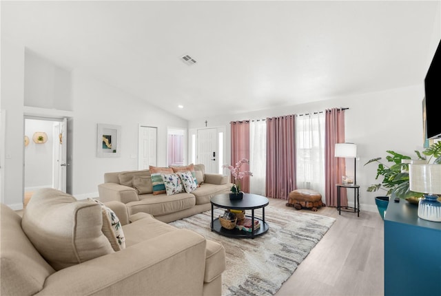 living area with high vaulted ceiling, light wood-type flooring, visible vents, and baseboards