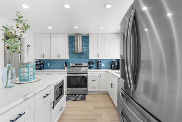 kitchen with wall chimney range hood, white cabinetry, appliances with stainless steel finishes, and light countertops