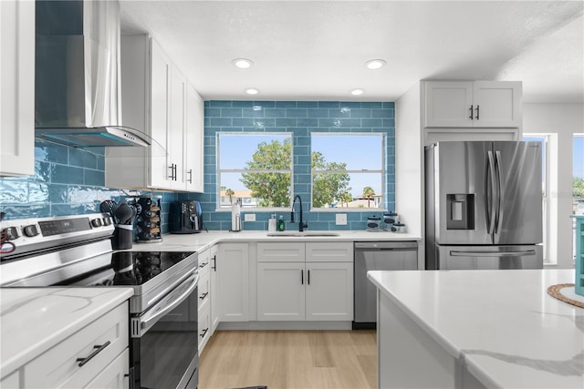 kitchen featuring appliances with stainless steel finishes, white cabinetry, a sink, and wall chimney exhaust hood