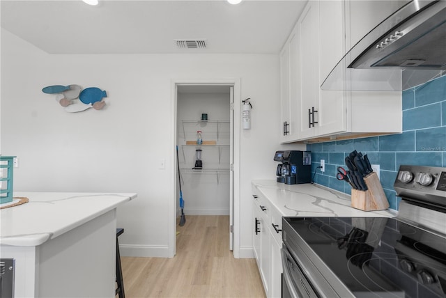 kitchen featuring visible vents, white cabinets, wall chimney exhaust hood, light stone countertops, and stainless steel electric range