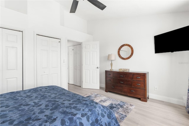 bedroom featuring high vaulted ceiling, ceiling fan, light wood-type flooring, and multiple closets