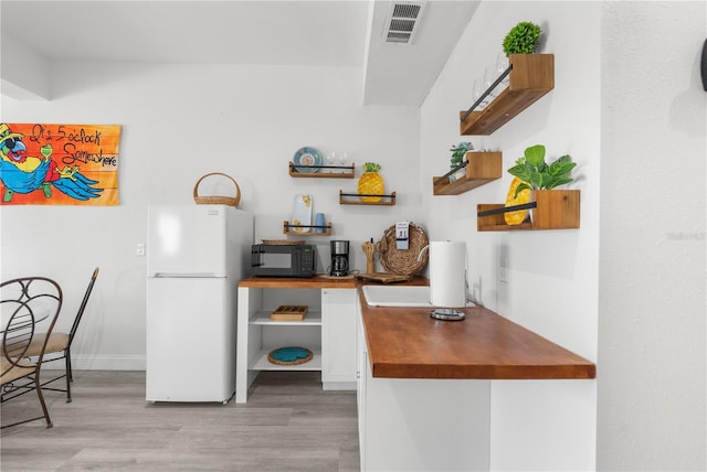 kitchen with visible vents, freestanding refrigerator, white cabinets, light wood-type flooring, and black microwave