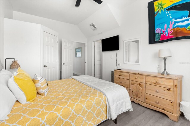 bedroom with a ceiling fan, visible vents, vaulted ceiling, and wood finished floors