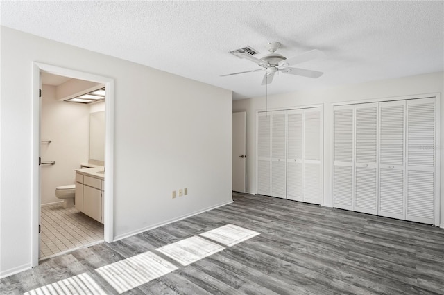 unfurnished bedroom with ceiling fan, wood-type flooring, connected bathroom, and two closets