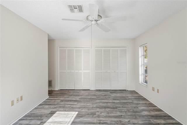 unfurnished bedroom with wood-type flooring, a textured ceiling, two closets, and ceiling fan