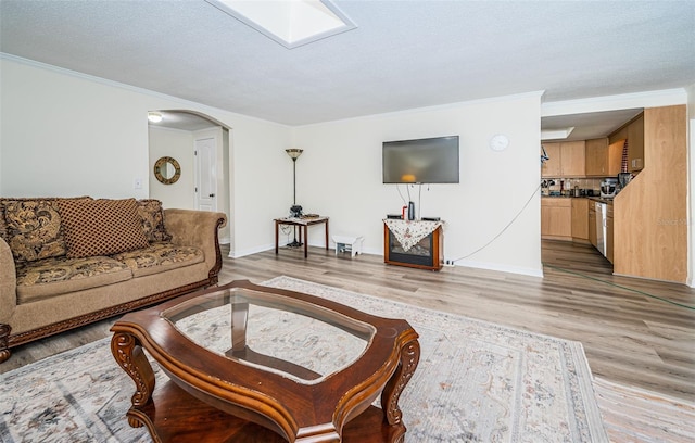 living room with a textured ceiling, ornamental molding, a skylight, and light hardwood / wood-style floors