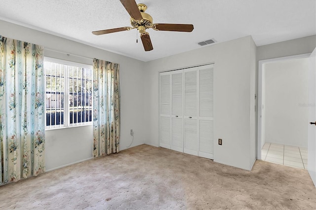 unfurnished bedroom featuring a textured ceiling, a closet, ceiling fan, and light carpet