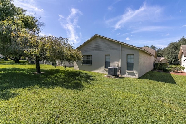 back of property featuring stucco siding, central AC unit, and a yard