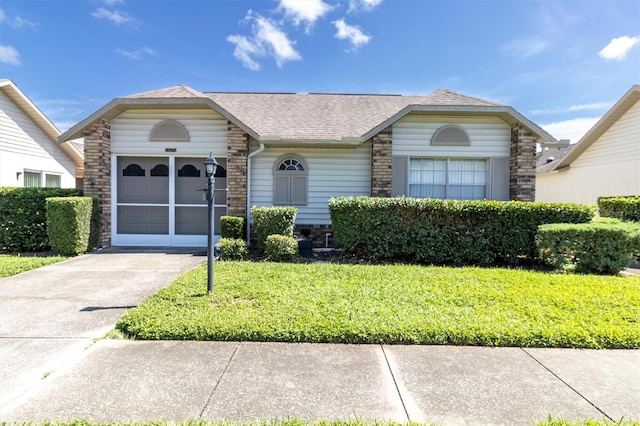 ranch-style house featuring driveway, brick siding, a shingled roof, an attached garage, and a front yard