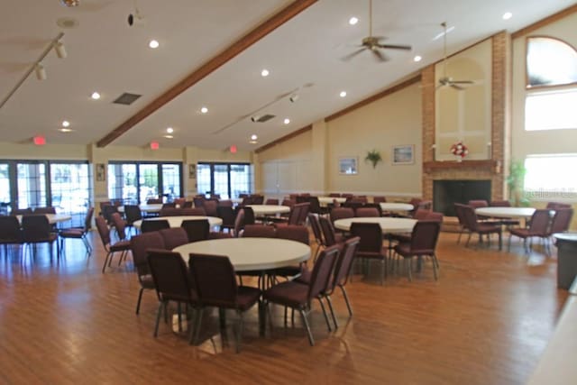 dining room with a fireplace, beamed ceiling, ceiling fan, wood-type flooring, and high vaulted ceiling